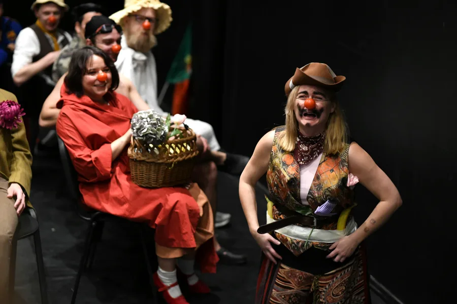 Two performers laughing together, one in red and one in a cowboy hat.